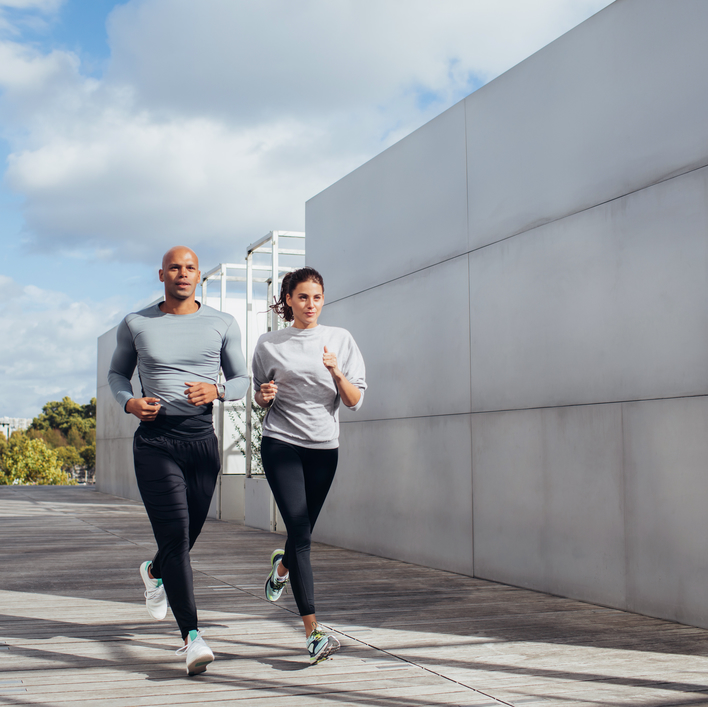 ein sportliches Pärchen läuft auf der Straße neben einem grauen Gebäude