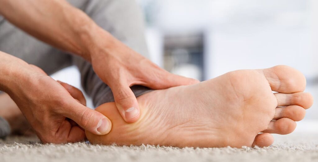 Mann massiert seine Ferse, da er Fersenschmerzen hat