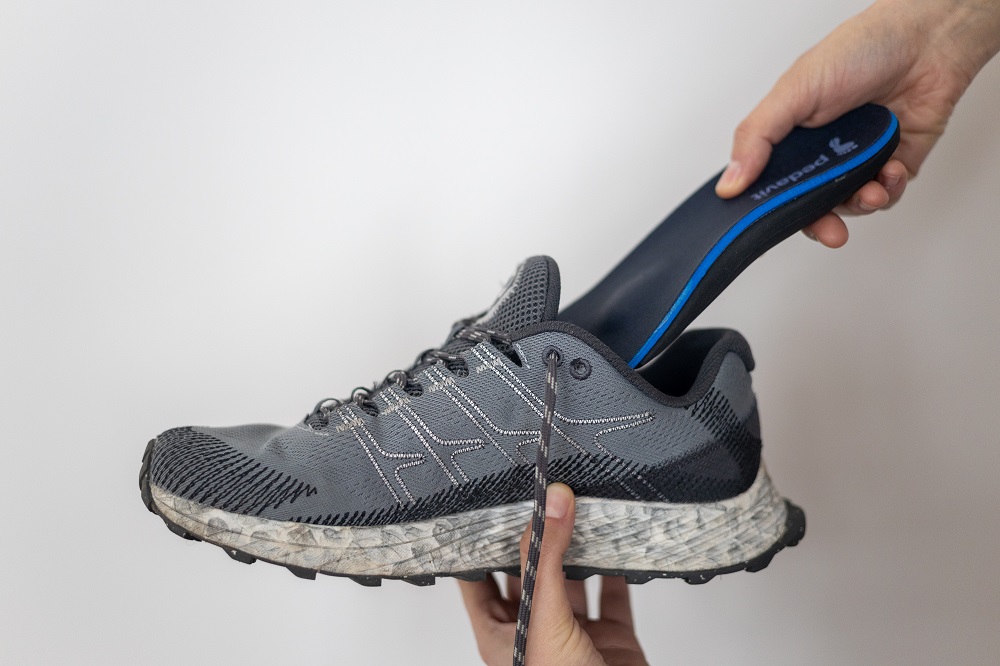 orthopädische Einlagen werden in einen grauen Sportschuh gesteckt.