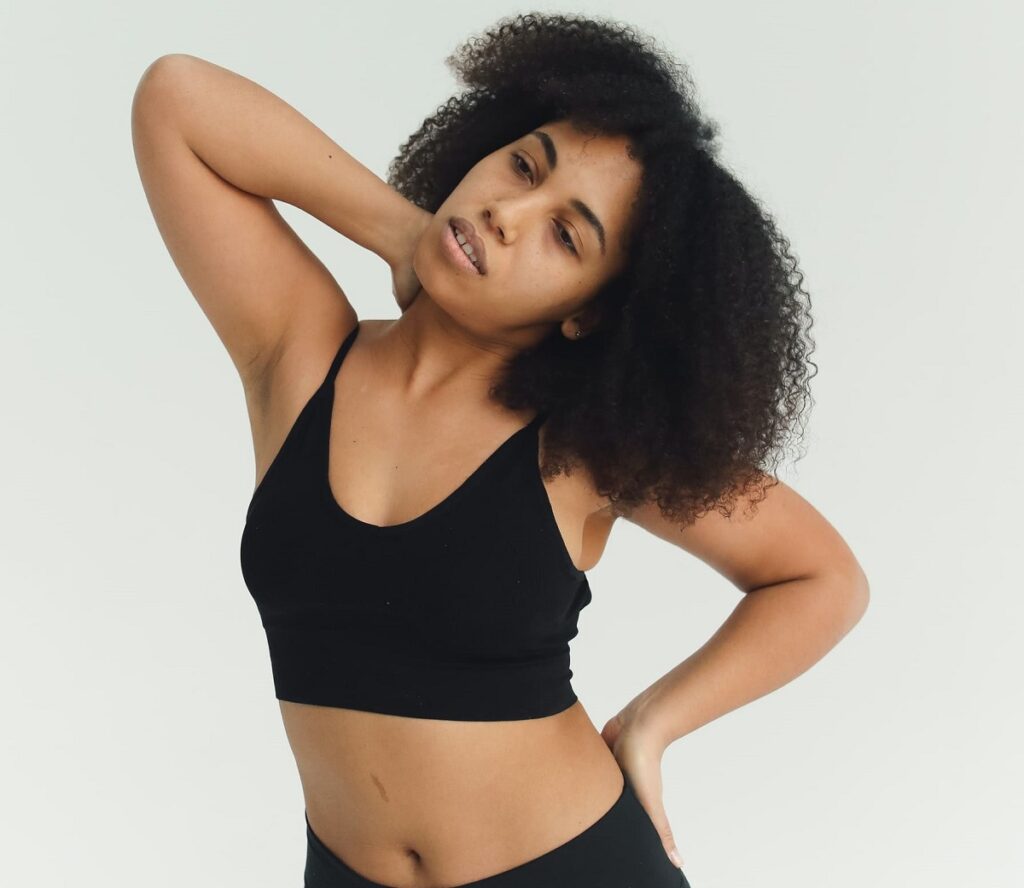 Frau dehnt ihr Nacken mit einem Arm, der andere Arm ist an der Hüfte.