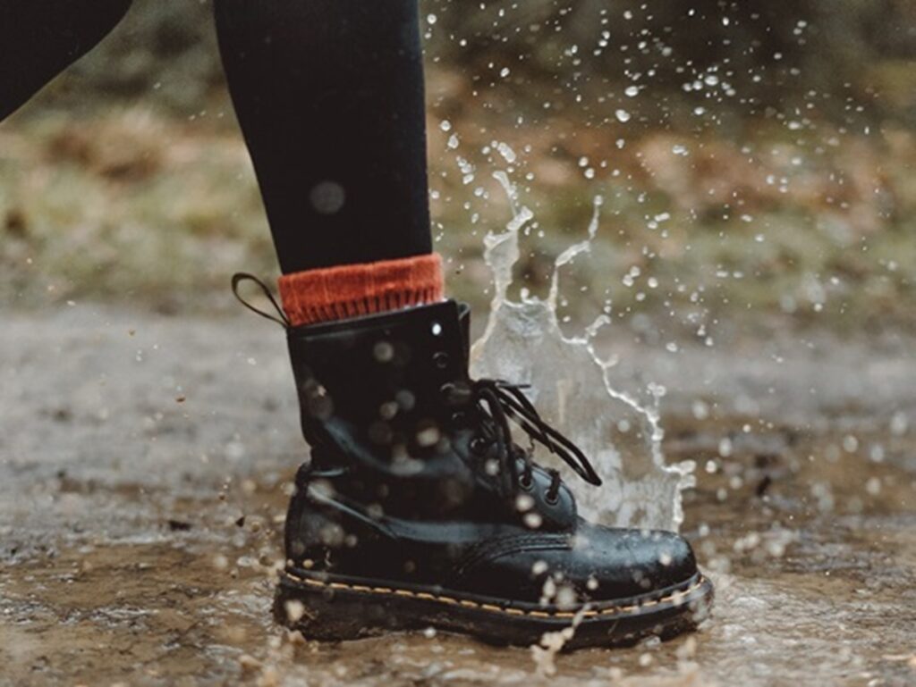 Schwarze Damenstiefel treten in eine Pfütze.